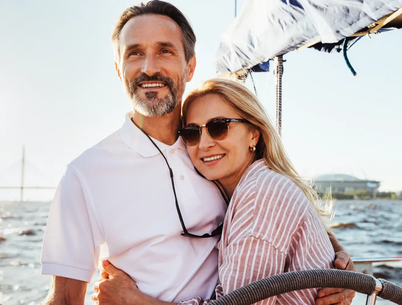 Una pareja madura, activa y sonriente disfruta de un paseo en barco bajo el sol, lo que representa salud y envejecer con salud.