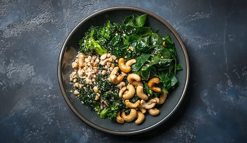 Des légumes verts à feuilles frais et des noix de cajou, deux excellents aliments riches en collagène pour les végétariens, présentés sur une table rustique en bois.