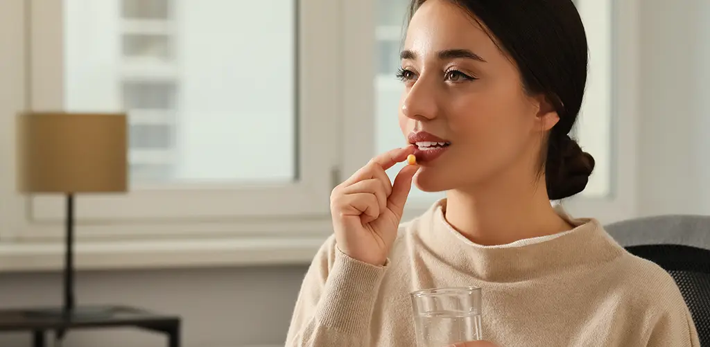 Une femme sourit alors qu'elle prend une capsule de supplément de spermidine, mettant en avant les avantages anti-âge et de longévité.