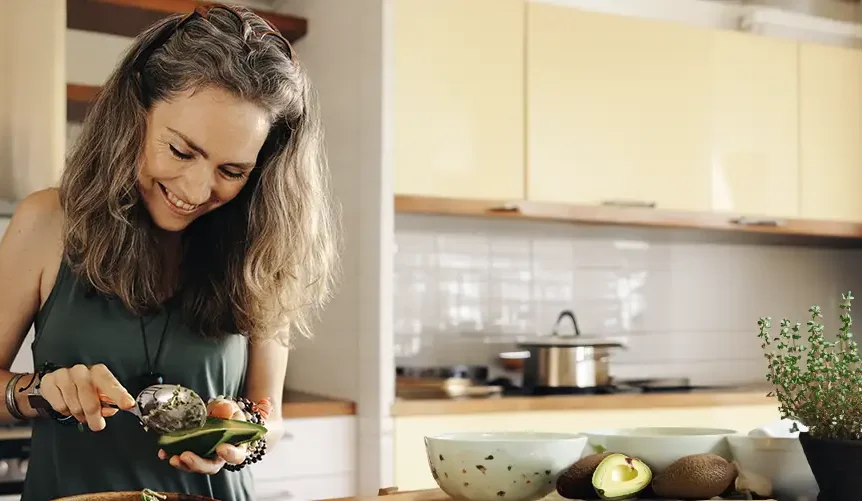 une femme souriante dans sa cuisine en train de préparer un avocat