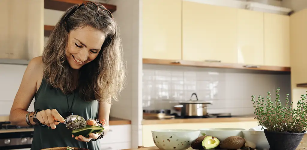 smiling woman in kitchen preparing avocado