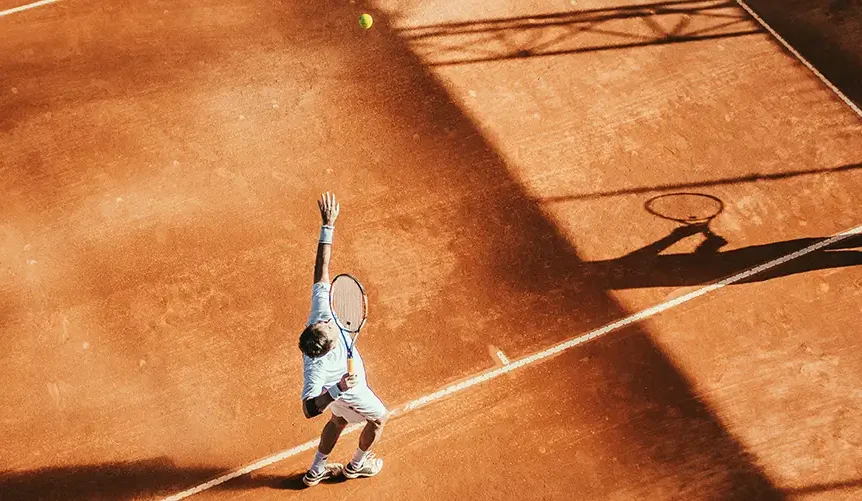 Man is playng tennins, tennis ball in the air ready to serve. High sun exposure. Bird's-eye view