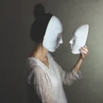 O femeie este fotografiată din profil purtând o mască albă, în timp ce ține în mâini o mască albă identică și se uită la ea. Ea poartă o rochie albă cu dantelă.
