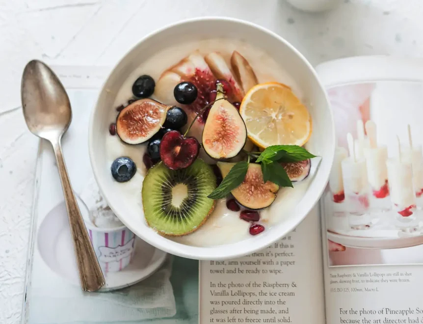 A bowl of yogurt topped with granola, banana slices, blueberries, and fruit jam.