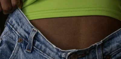 Persoon draagt een blauwe spijkerbroek die de tailleband van de buik wegtrekt, met een groen topje zichtbaar.