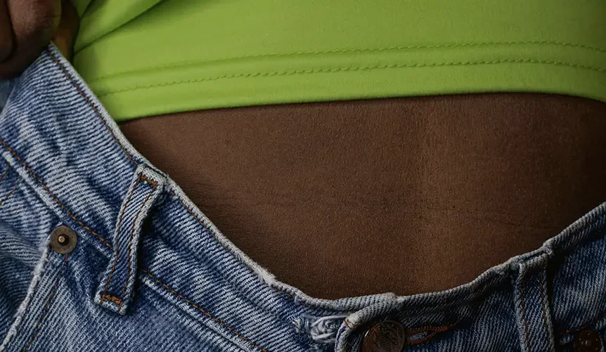 En person iført blå jeans, der trækker linningen væk fra maven, så en grøn bluse kan ses.