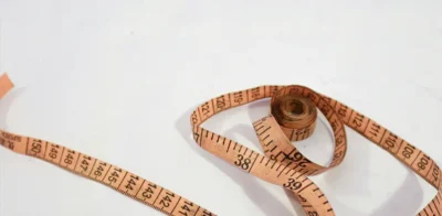 An orange measuring tape rolled up on a white surface, symbolizing body measurements, weight management, or tracking changes in body composition.