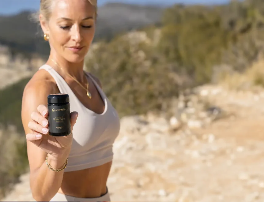 Woman outdoors holding a dark bottle of Purovitalis Liposomal Resveratrol supplement in front of a sunny mountain background