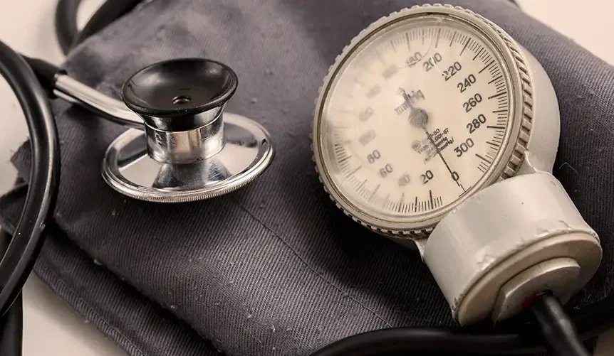 Blodtryksmanchet med analogt manometer og et stetoskop på en hvid overflade, brugt til at måle blodtryk.