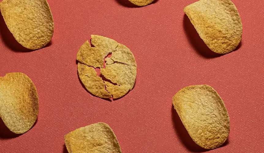 Pattern of potato chips scattered on a red background, with one broken chip in the center standing out from the others.