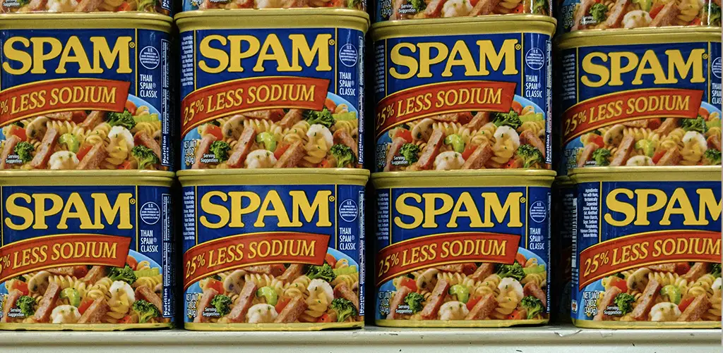 Lattine di SPAM «25% di sodio in meno» allineate su uno scaffale del supermercato.