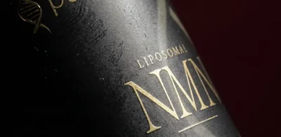 Close-up of a black Purovitalis Liposomal NMN supplement bottle with gold lettering and a dark red background.