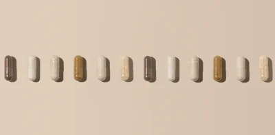 A row of different supplement capsules arranged in a straight line on a soft beige background, representing longevity and wellness supplements.
