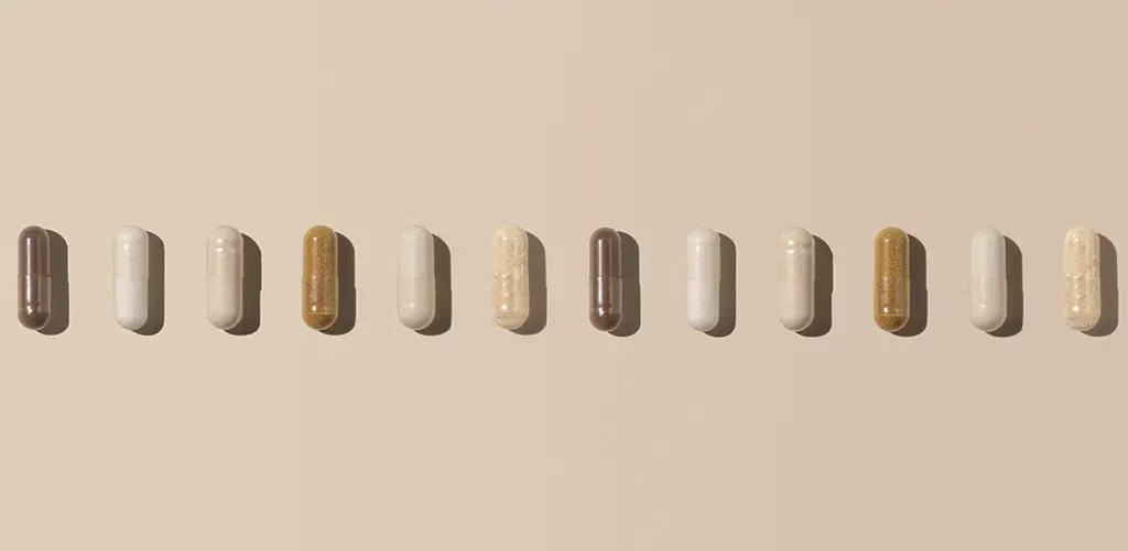 A row of different supplement capsules arranged in a straight line on a soft beige background, representing longevity and wellness supplements.