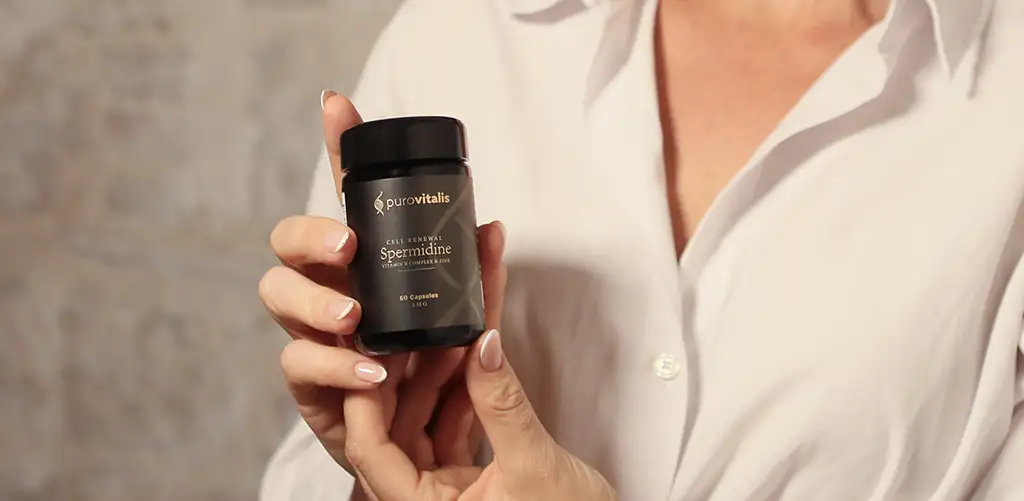 Person holding a bottle of Purovitalis Spermidine supplement in front of a neutral background, highlighting the liposomal longevity formula and premium packaging.