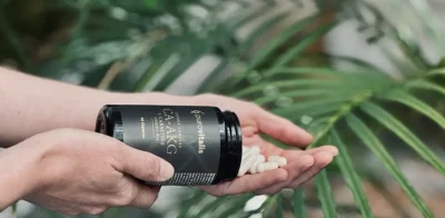 Iemand die Purovitalis Ca-AKG-capsules met L-carnitine en vitamine B12 in zijn hand giet, waarbij de nadruk ligt op longevity ondersteuning van de celenergie.