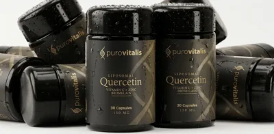 Multiple black bottles of Purovitalis Liposomal Quercetin supplements with gold lettering, highlighting added ingredients Vitamin C, Zinc, and Bromelain, scattered against a light background with water droplets on the packaging.