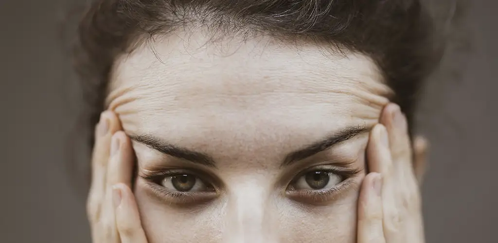 Close-up of a middle-aged woman touching her forehead showing fine lines and skin changes during menopause